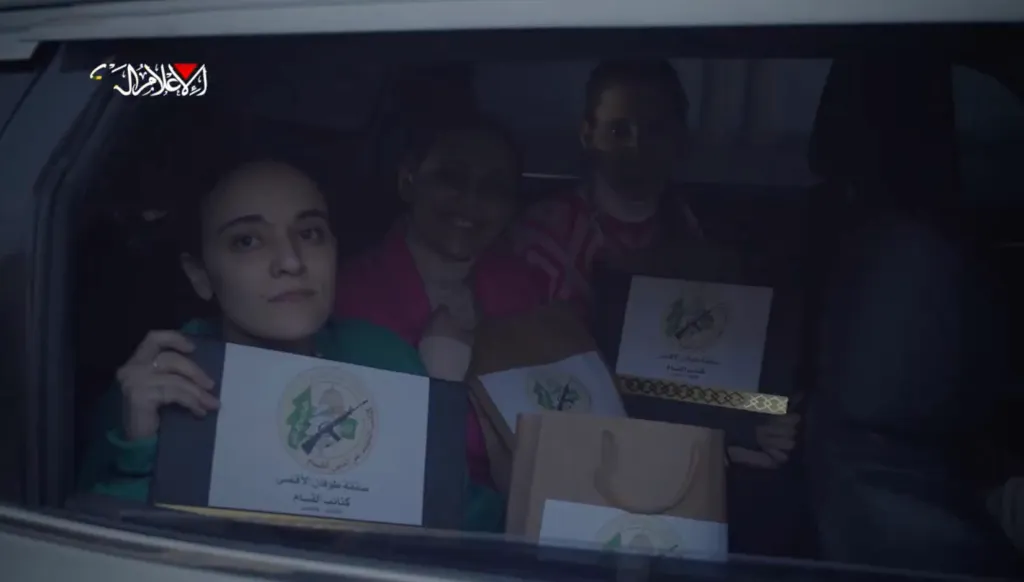 Three people in a car holding bags and boxes with the logo of the Al-Qassam Brigades.